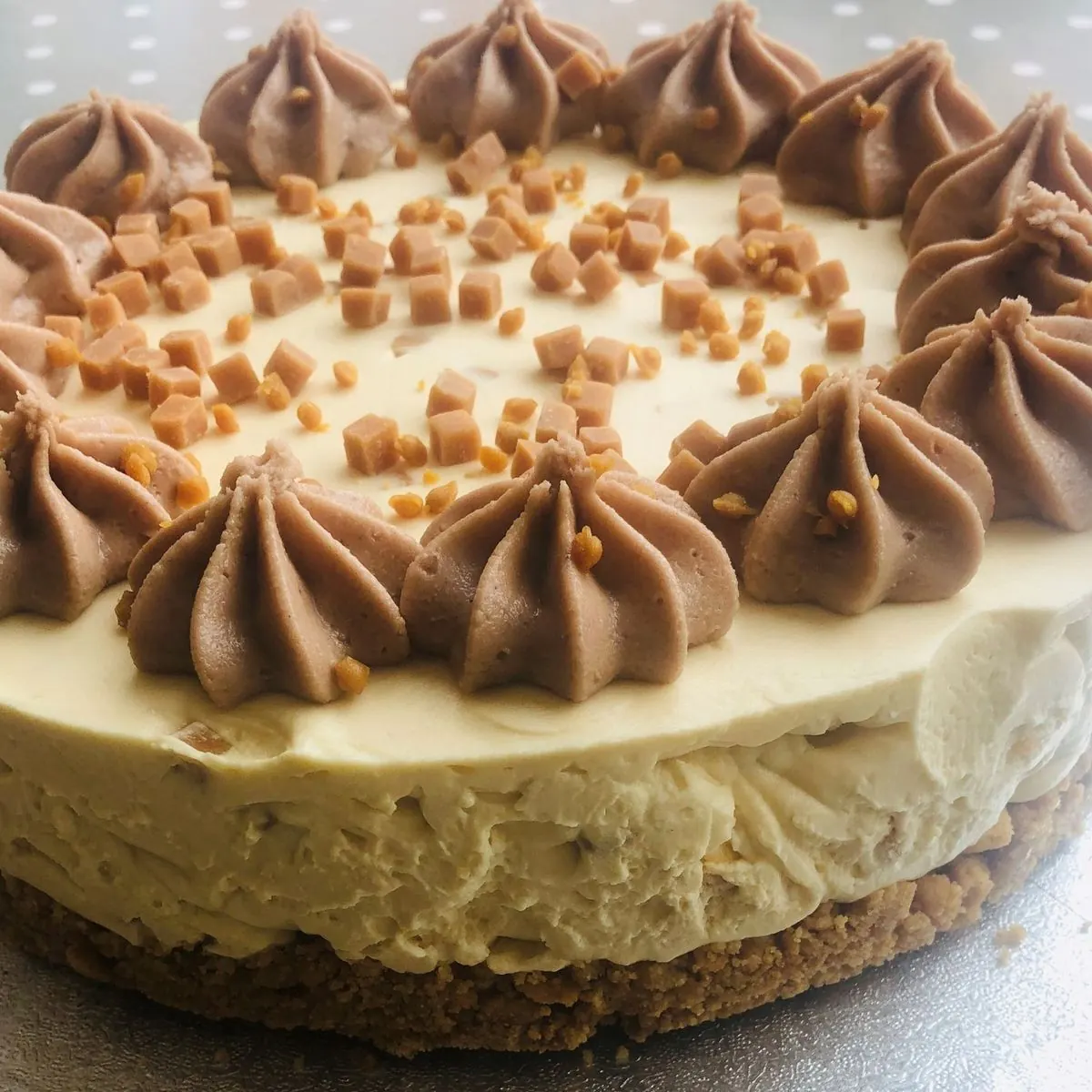 Whole caramel cheesecake ringed with piped chocolate swirls and fudge pieces