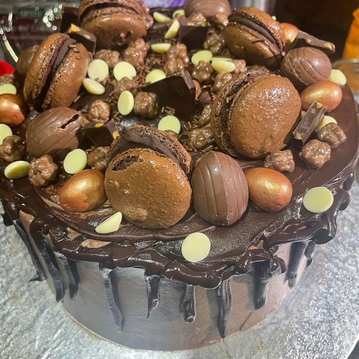 Chocolate drip cake topped with chocolate macarons, gold eggs and white chocolate buttons