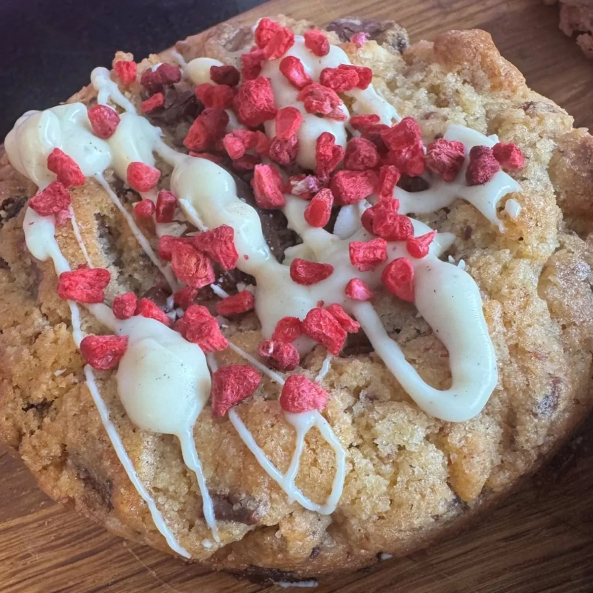 A thick cookie drizzled with white chocolate and scattered with raspberry pieces