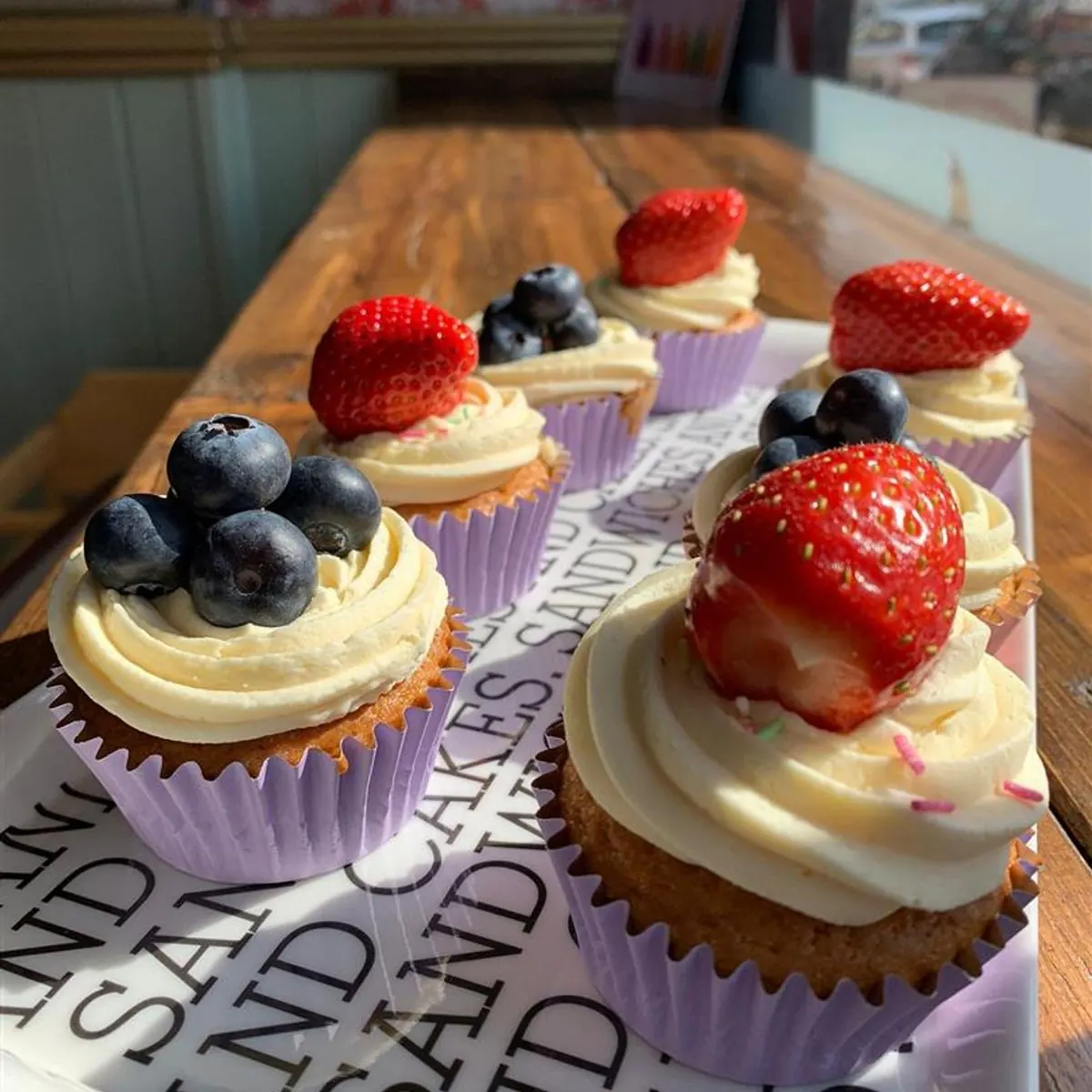 Vanilla cupcakes in lilac cases topped with buttercream, strawberries and blueberries